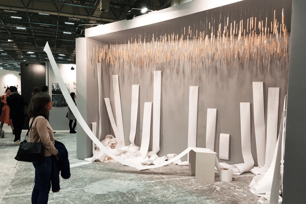 Visitor in front of Contents / İçindekiler, a wall of pencils with paper strips piled on the floor