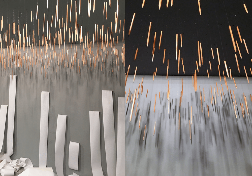 Paper strips hanging from rows of pencils fixed to the wall in Contents / İçindekiler