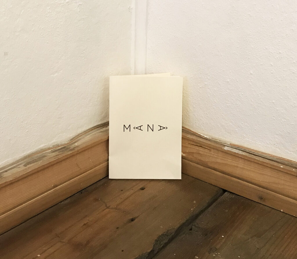 Small booklet titled MANA leaning against the wall in the corner of the room