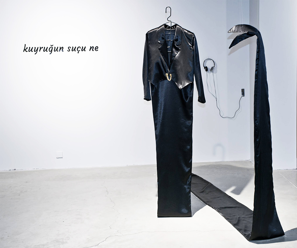 Installation kuyruk / tail: black jacket with a long tail-like strip and the wall text kuyruğun suçu ne