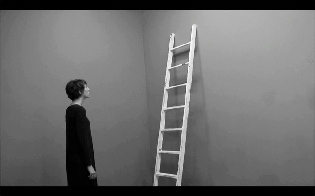 The artist facing a ladder leaning against a grey wall in the video Method