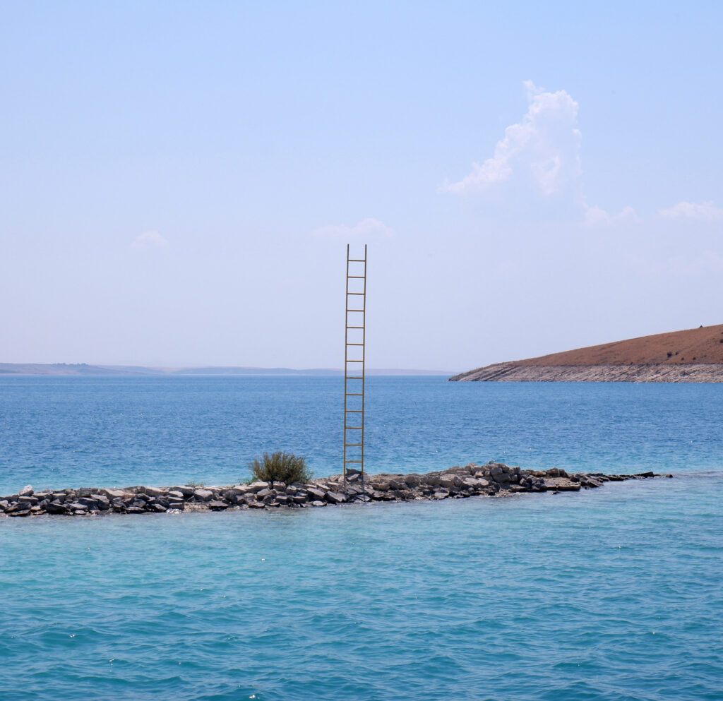 Installation Rising: a wooden ladder rising from a stone islet in the dam lake at the foot of Mount Nemrut