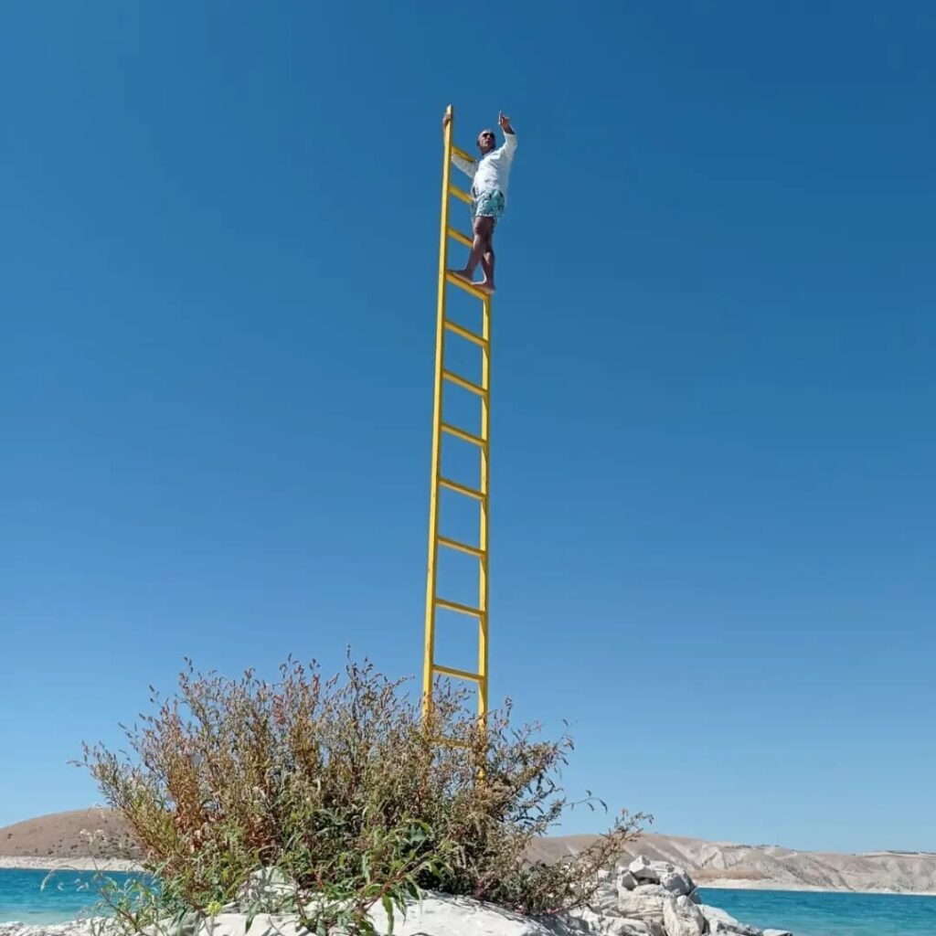 Person climbing the yellow ladder of Rising against a blue sky