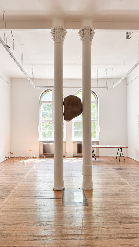 Amorphous brown form suspended between two white columns, yamukluk / amorphous