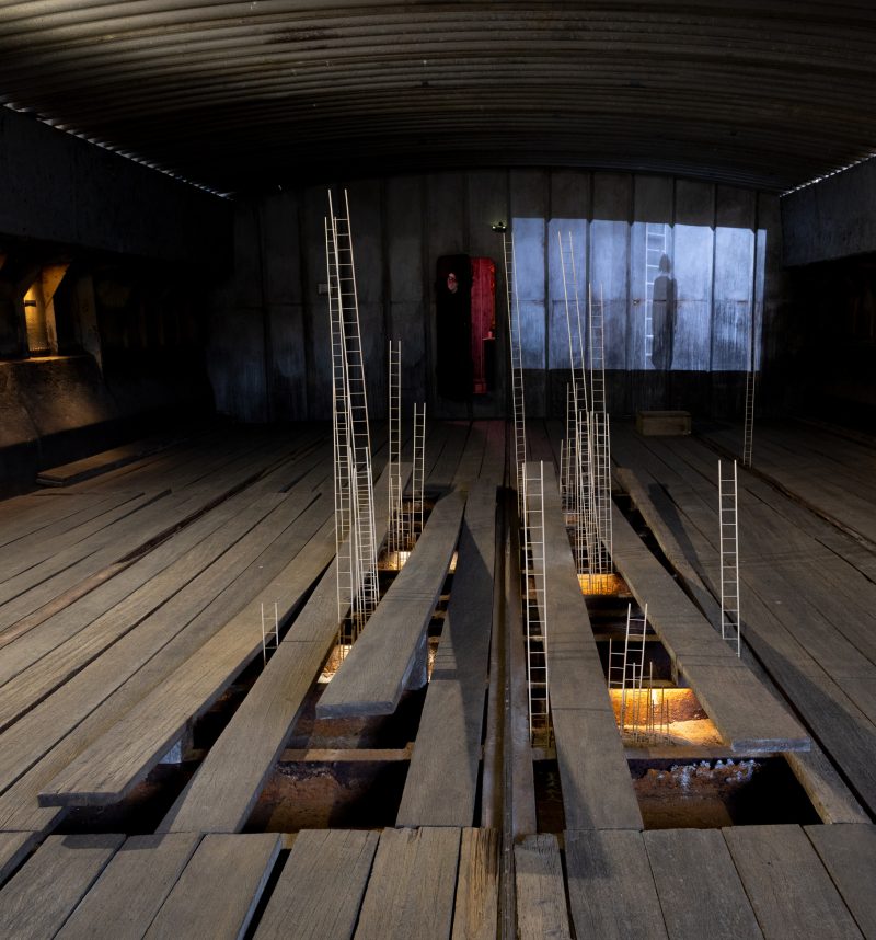 Exhibition view of An Address That is Waiting at Hošek Contemporary, Berlin: ladders rising from a wooden floor towards a lit panel